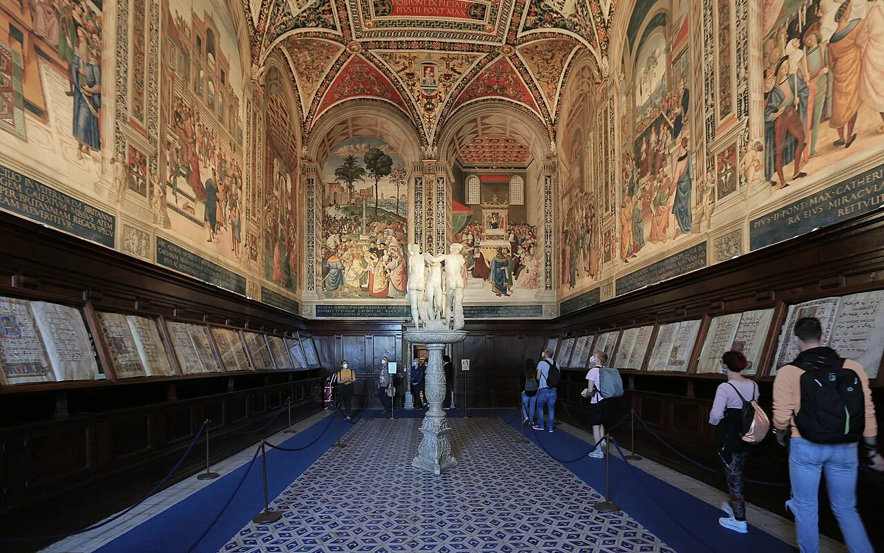 Inside the Piccolomini Library in Siena Cathedral, with painted fresco walls, a decorated vault and the marble Three Graces statue in the centre