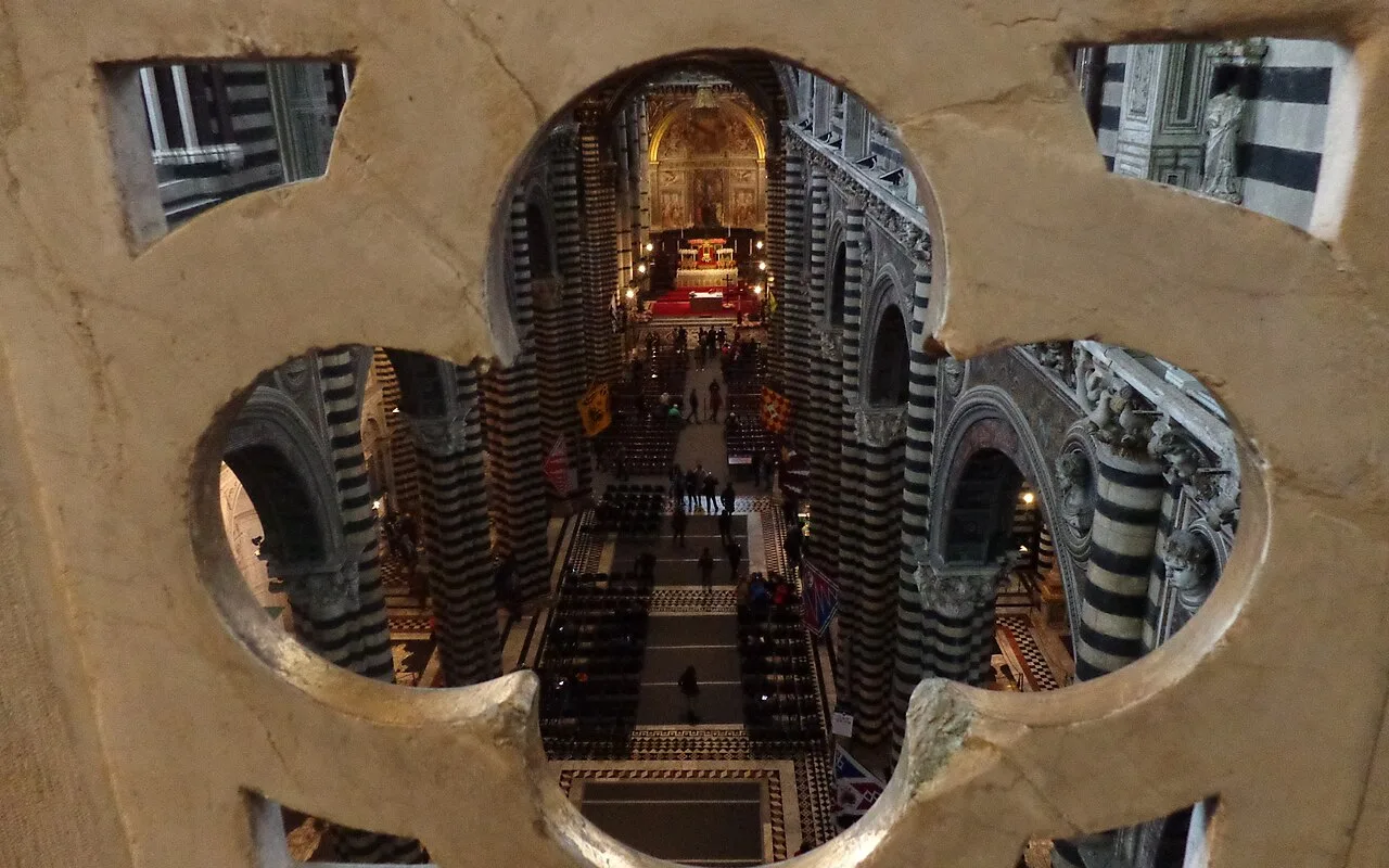 View through a stone quatrefoil in the upper gallery, straight down into the striped nave of Siena Cathedral